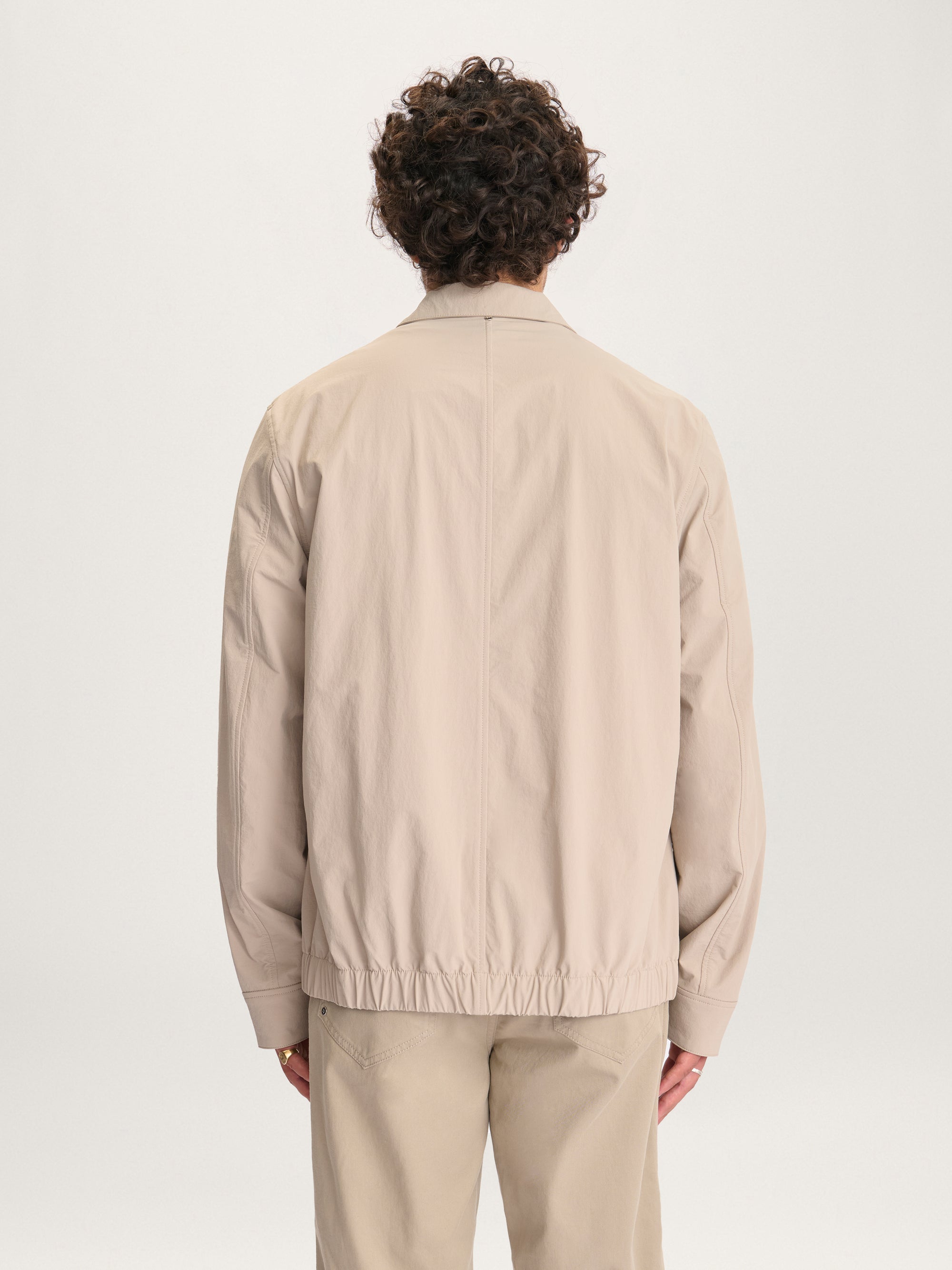 Back view of man wearing the Lestrange London 360 Jacket in beige showing elasticated hem detail