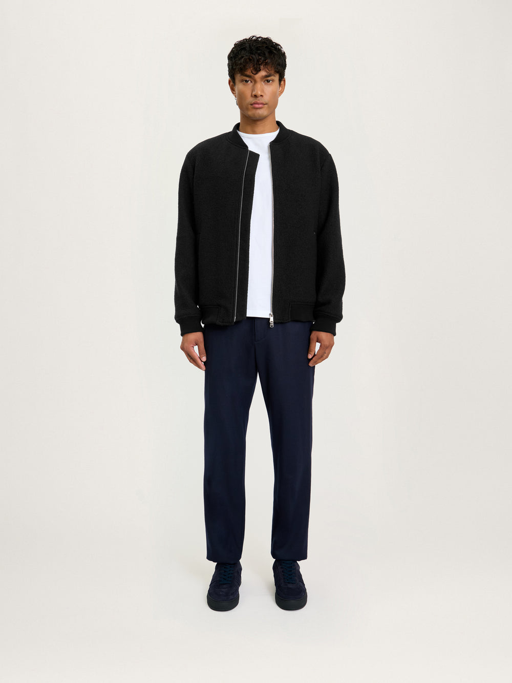 Model wearing the Lestrange London Cloud Wool Bomber in black, styled with navy trousers and a white T-shirt — full front view.