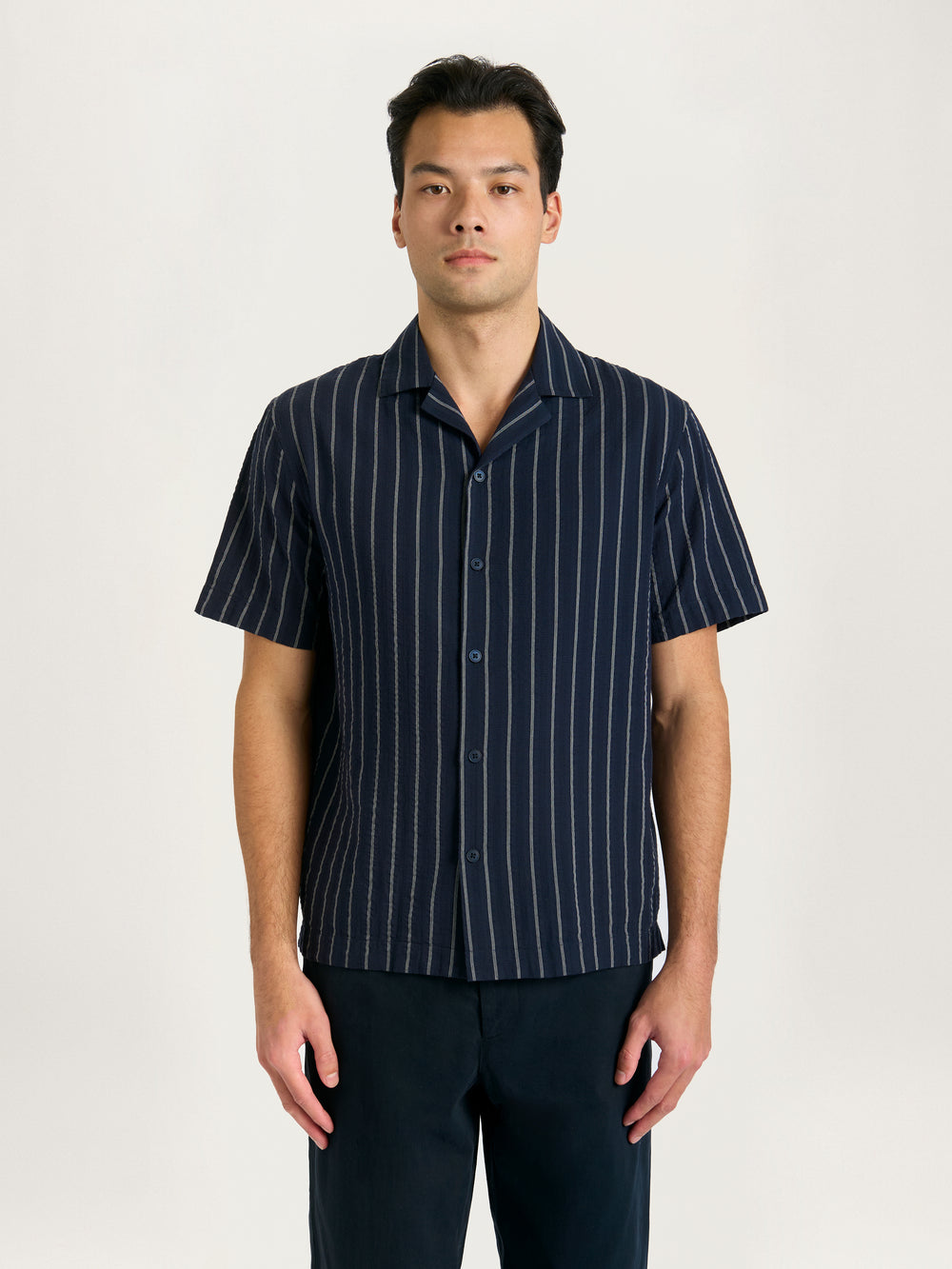 A male model wearing a navy striped cotton shirt with a relaxed fit.