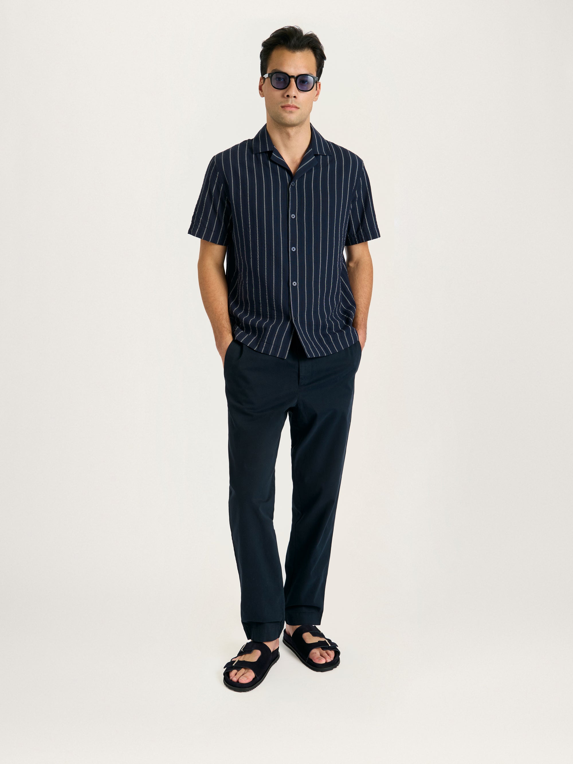Men’s navy striped Cuban collar shirt styled with tailored trousers and casual sandals.