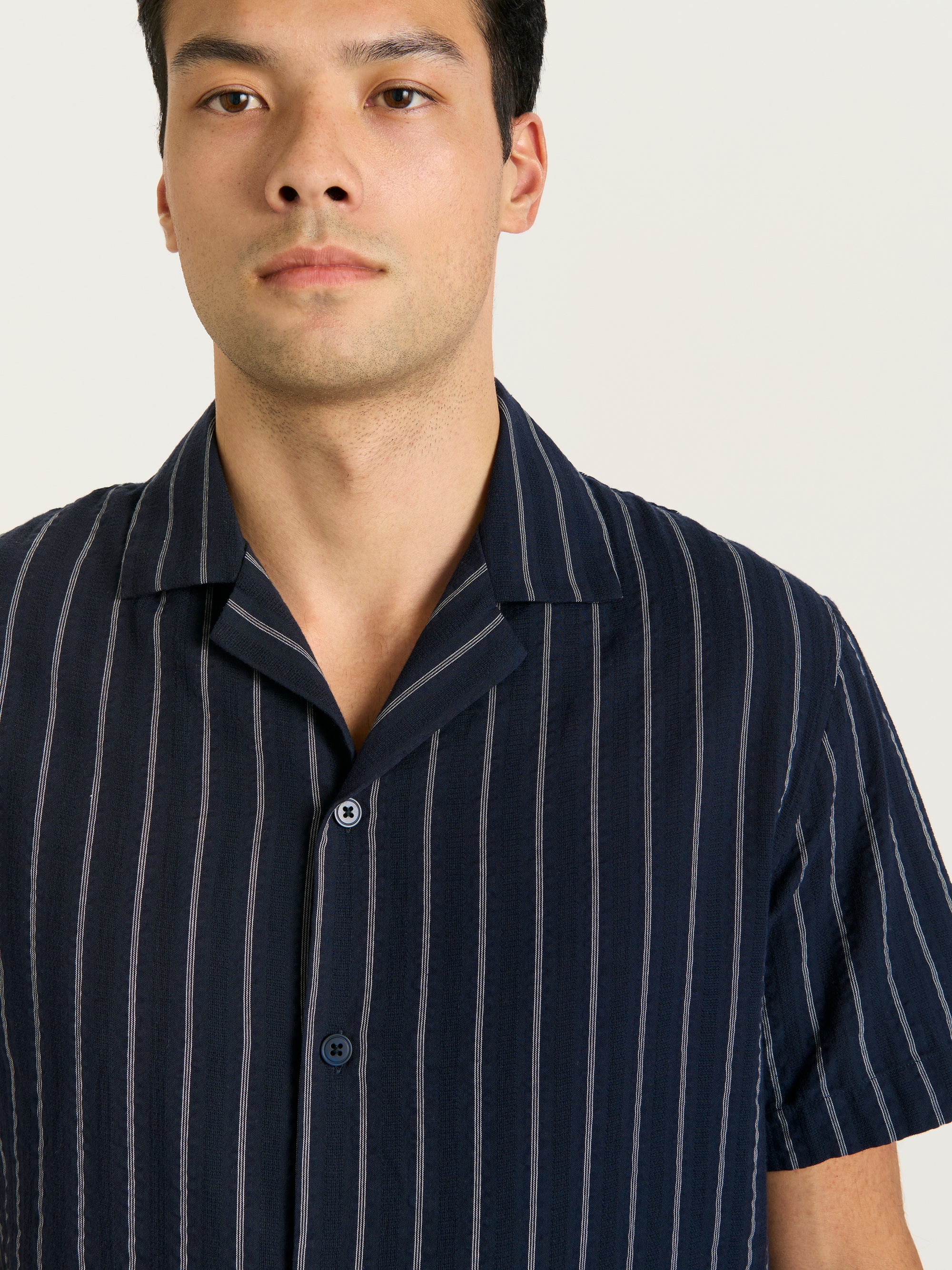 Detail view of men’s navy Cuban collar shirt with vertical white stripes and button front