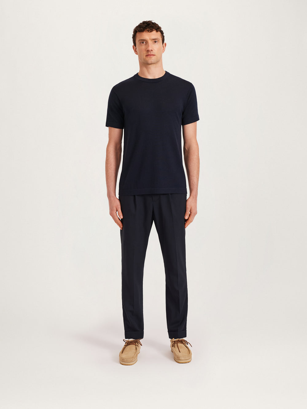 Men’s navy knitted T-shirt styled with navy tailored trousers and beige suede shoes – Lestrange London