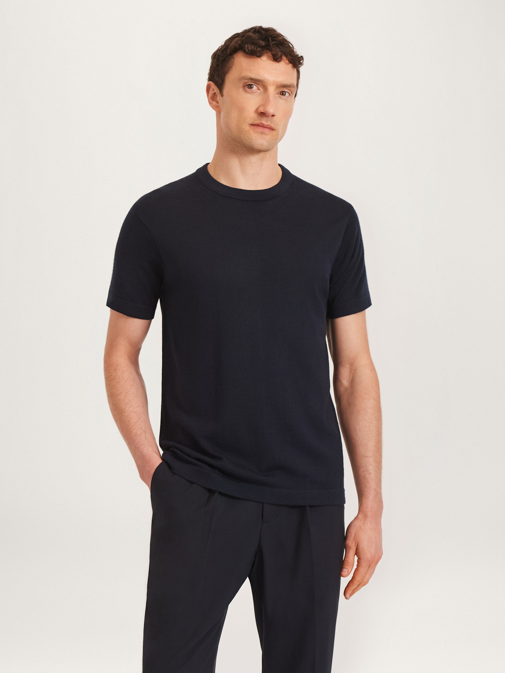 A man wearing a navy merino wool knit tee with short sleeves, paired with dark pants.