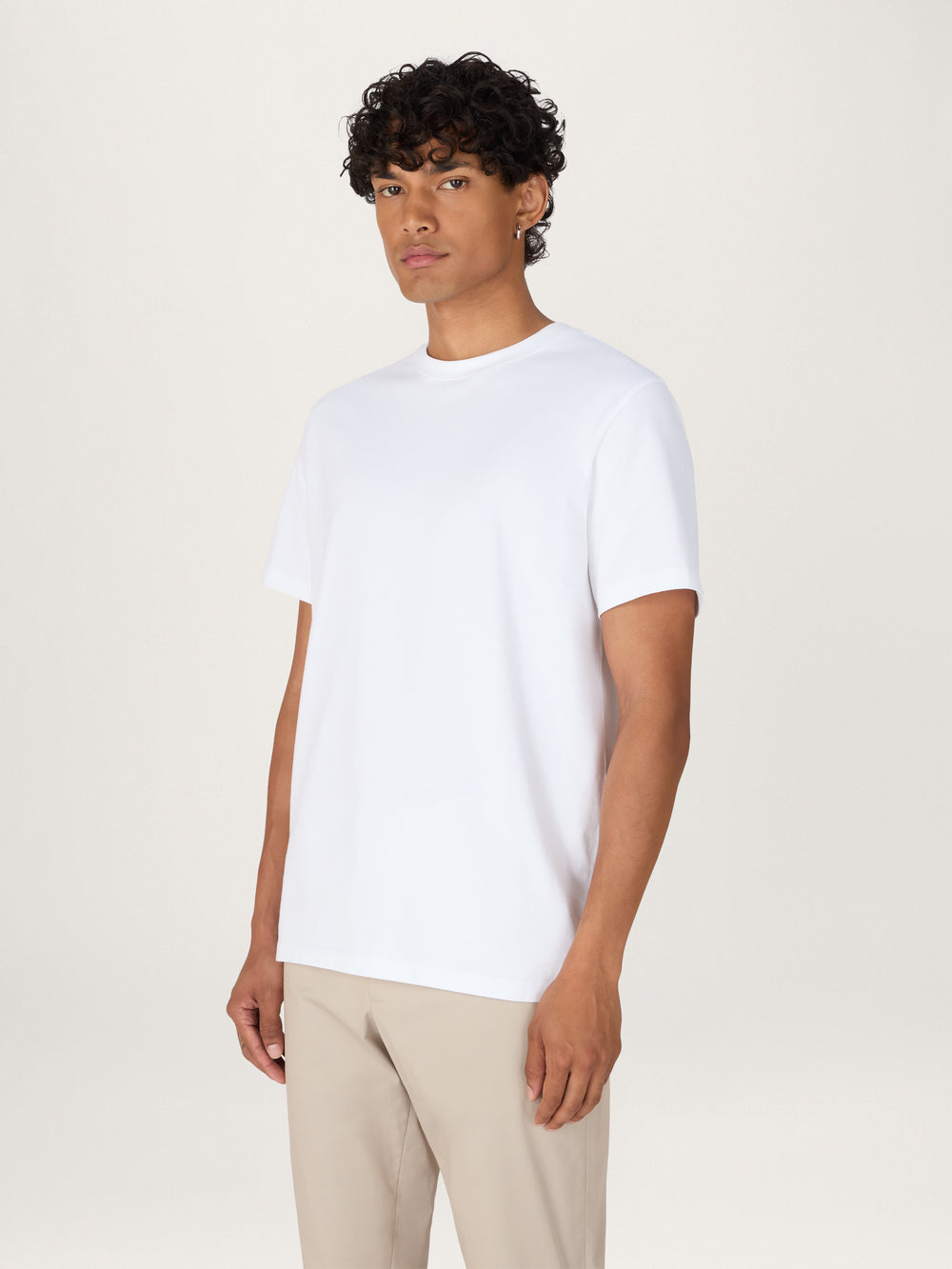 A person wearing a white, heavyweight organic cotton t-shirt with ribbed neck and side seam splits, paired with beige trousers.