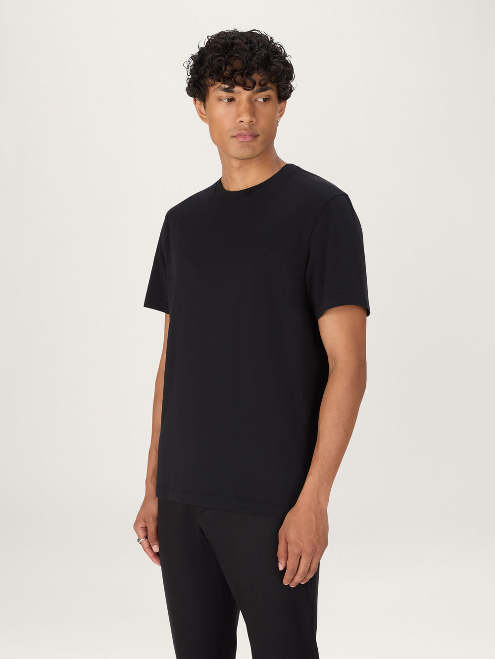 A person wearing a black, heavyweight organic cotton t-shirt with ribbed neck and side seam splits.
