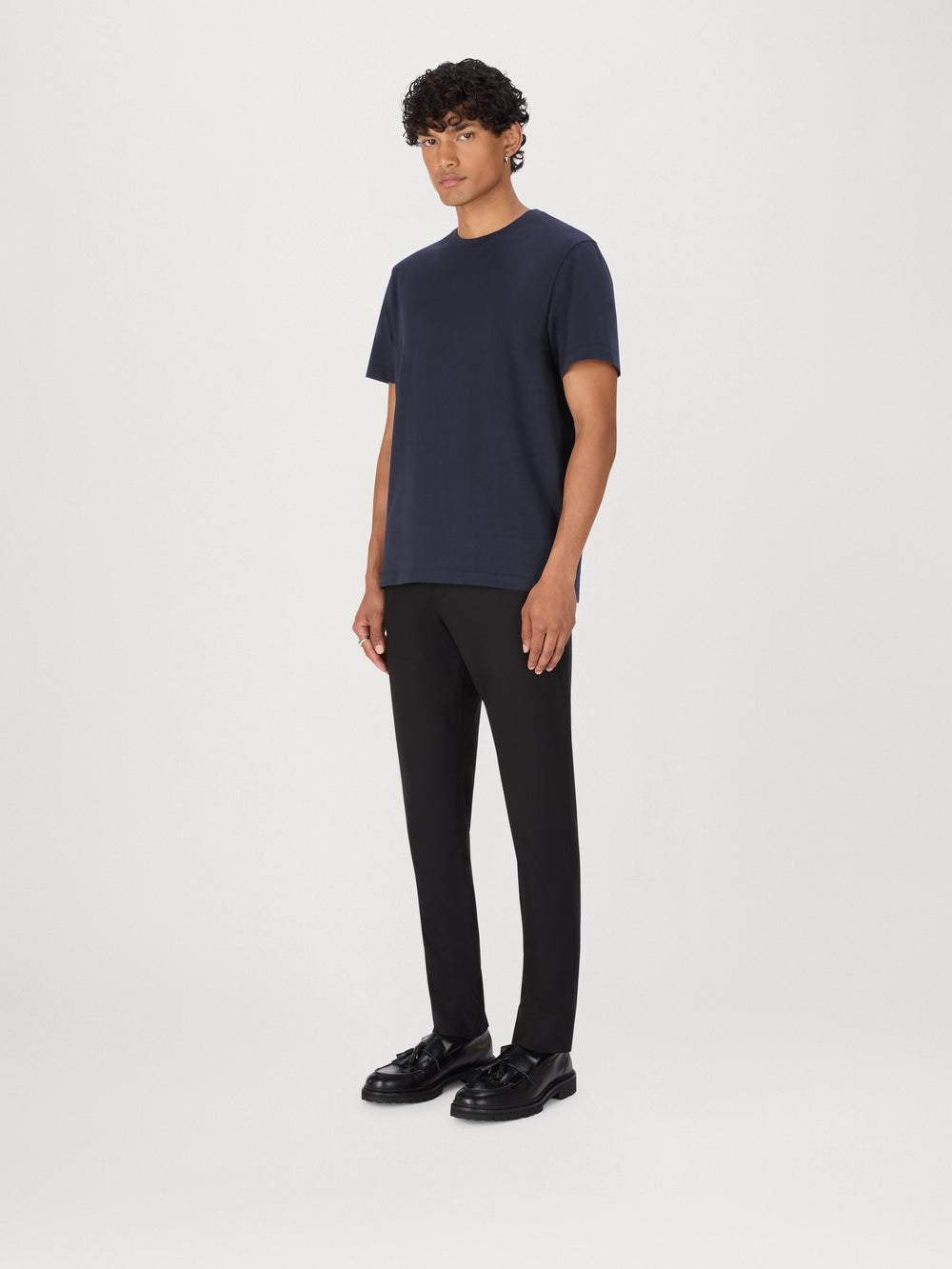 Person wearing a navy t-shirt, black pants, and black shoes on a white background