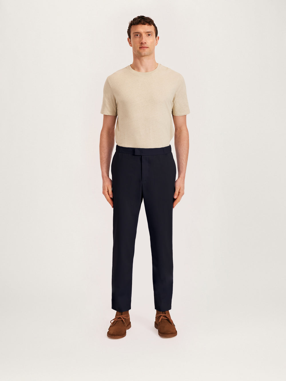 Man wearing a beige short-sleeve T-shirt with navy relaxed tropical wool trousers and brown suede shoes – smart casual menswear outfit