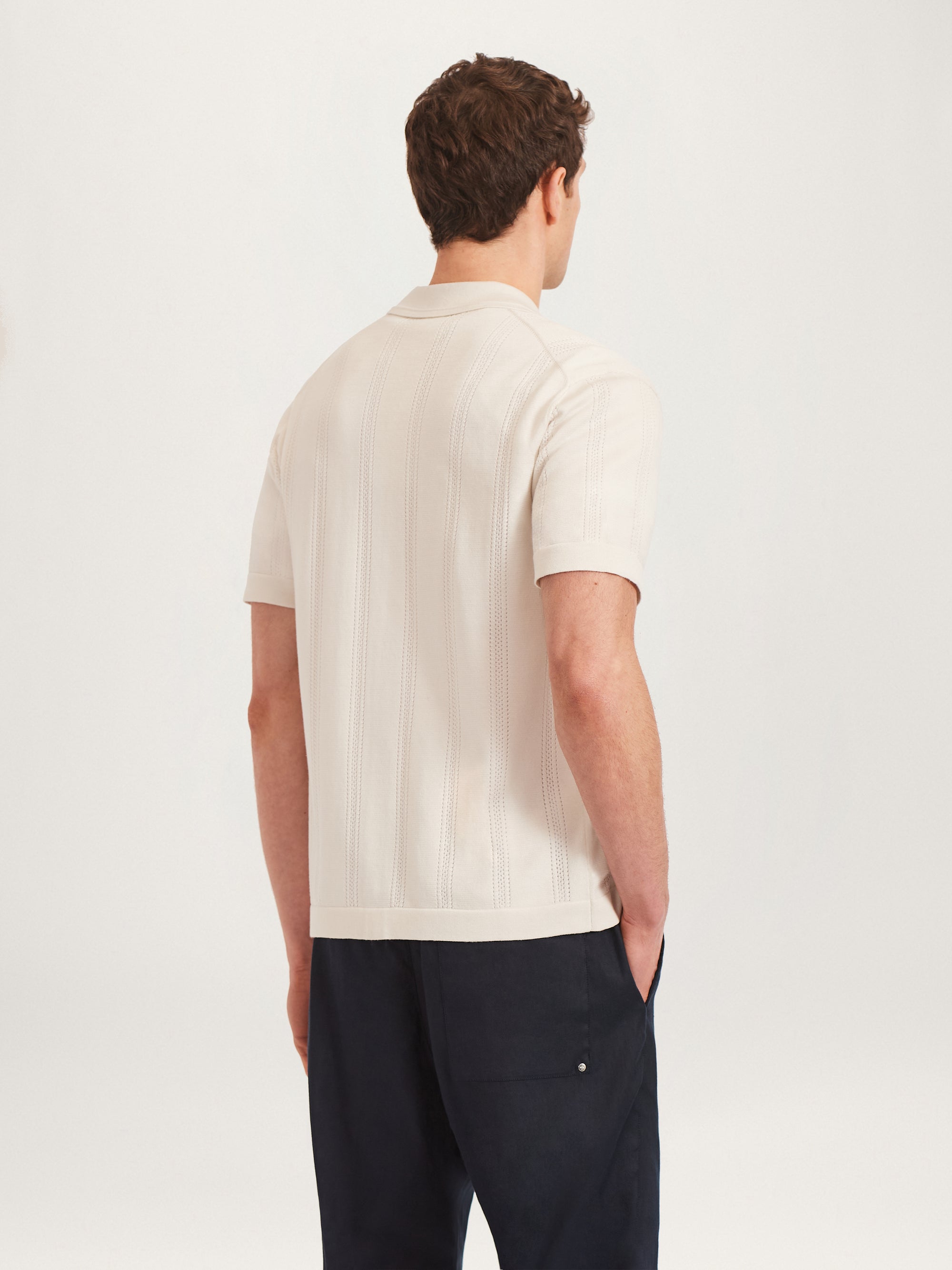 Back view of men’s textured knit shirt in ecru with short sleeves, styled with navy trousers – Lestrange London