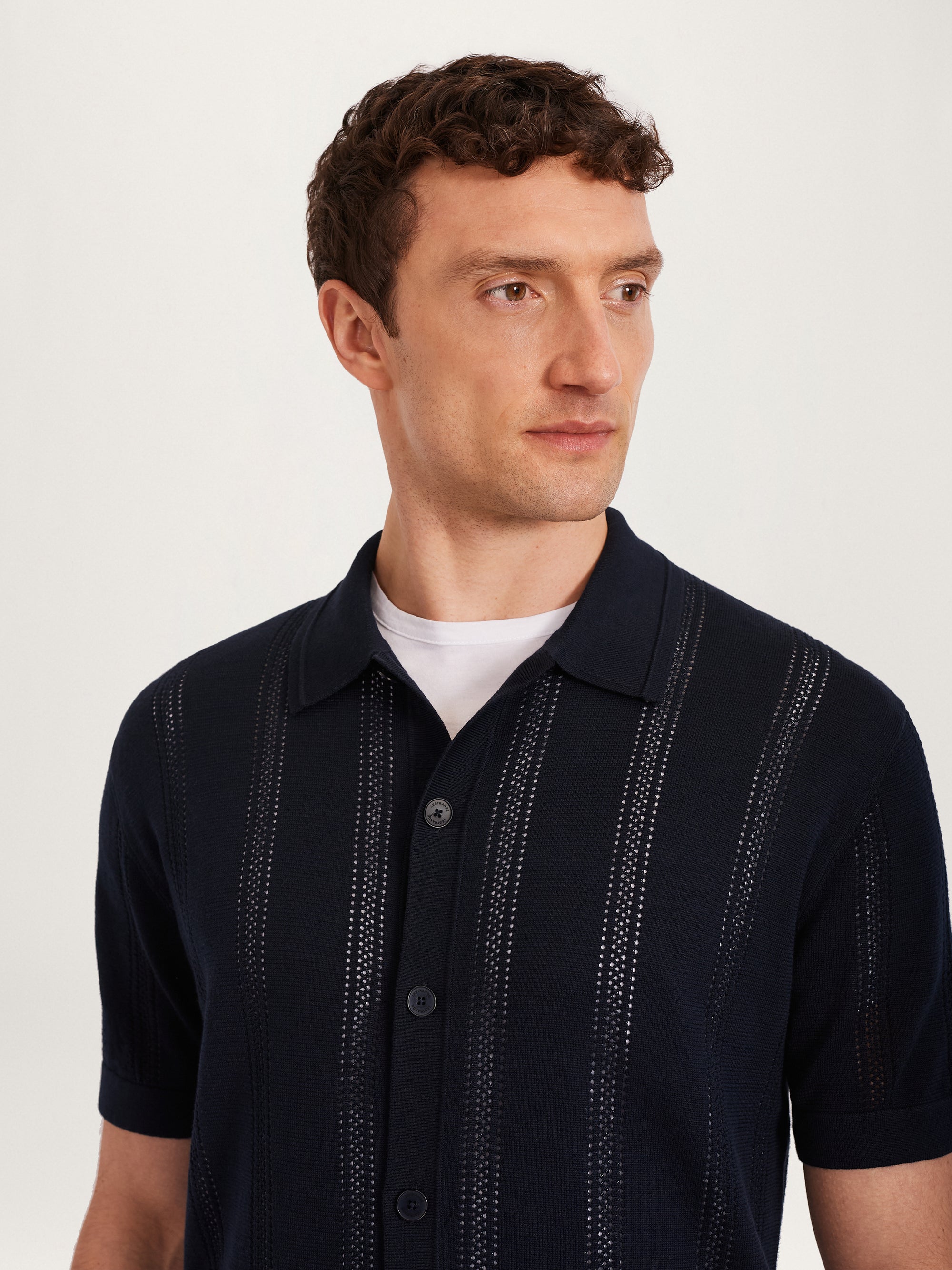 Close-up of men’s textured knit shirt in navy with short sleeves and button front, styled with a white undershirt – Lestrange London