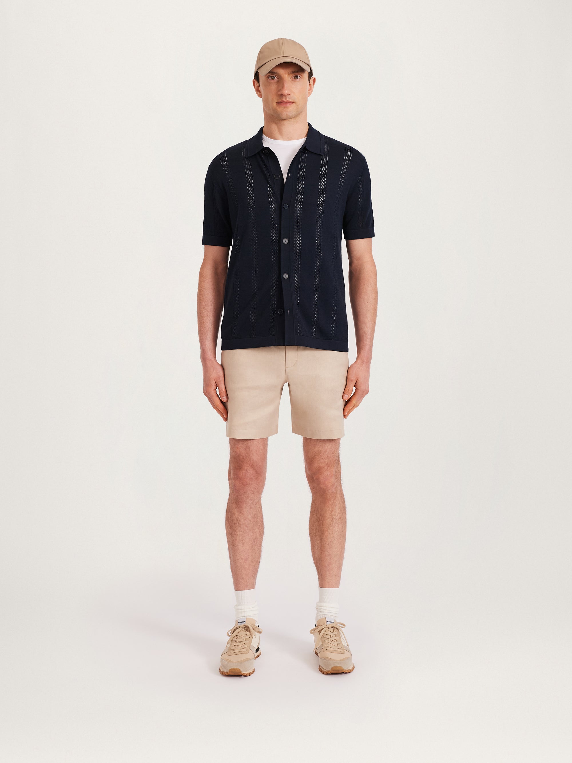 Front view of men’s textured knit shirt in navy with short sleeves, styled with beige shorts, sneakers, and a cap – Lestrange London