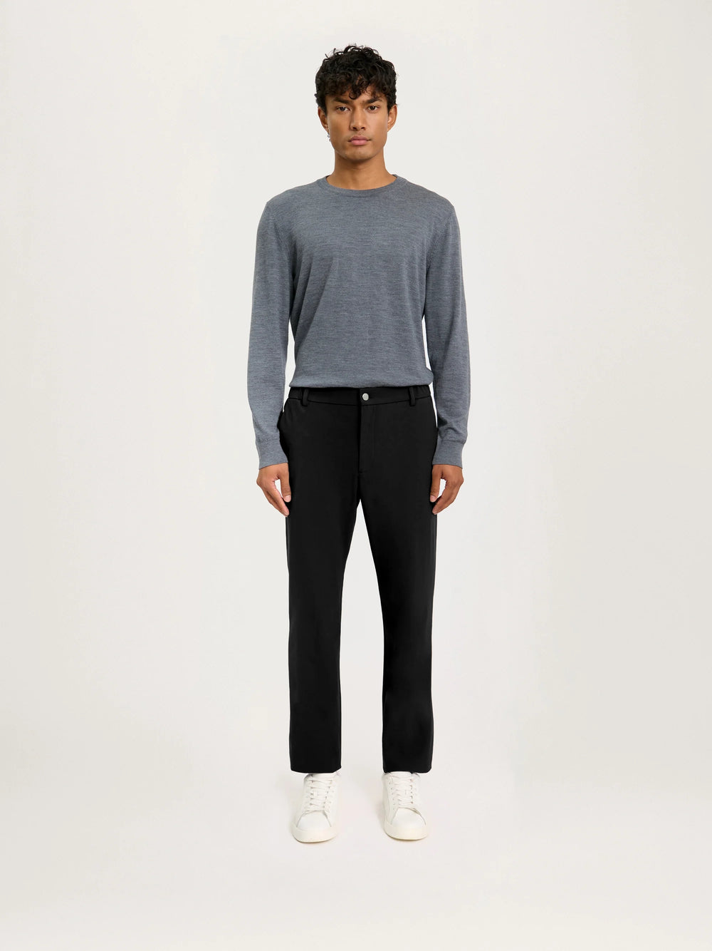 Person wearing a gray sweater and black pants on a white background