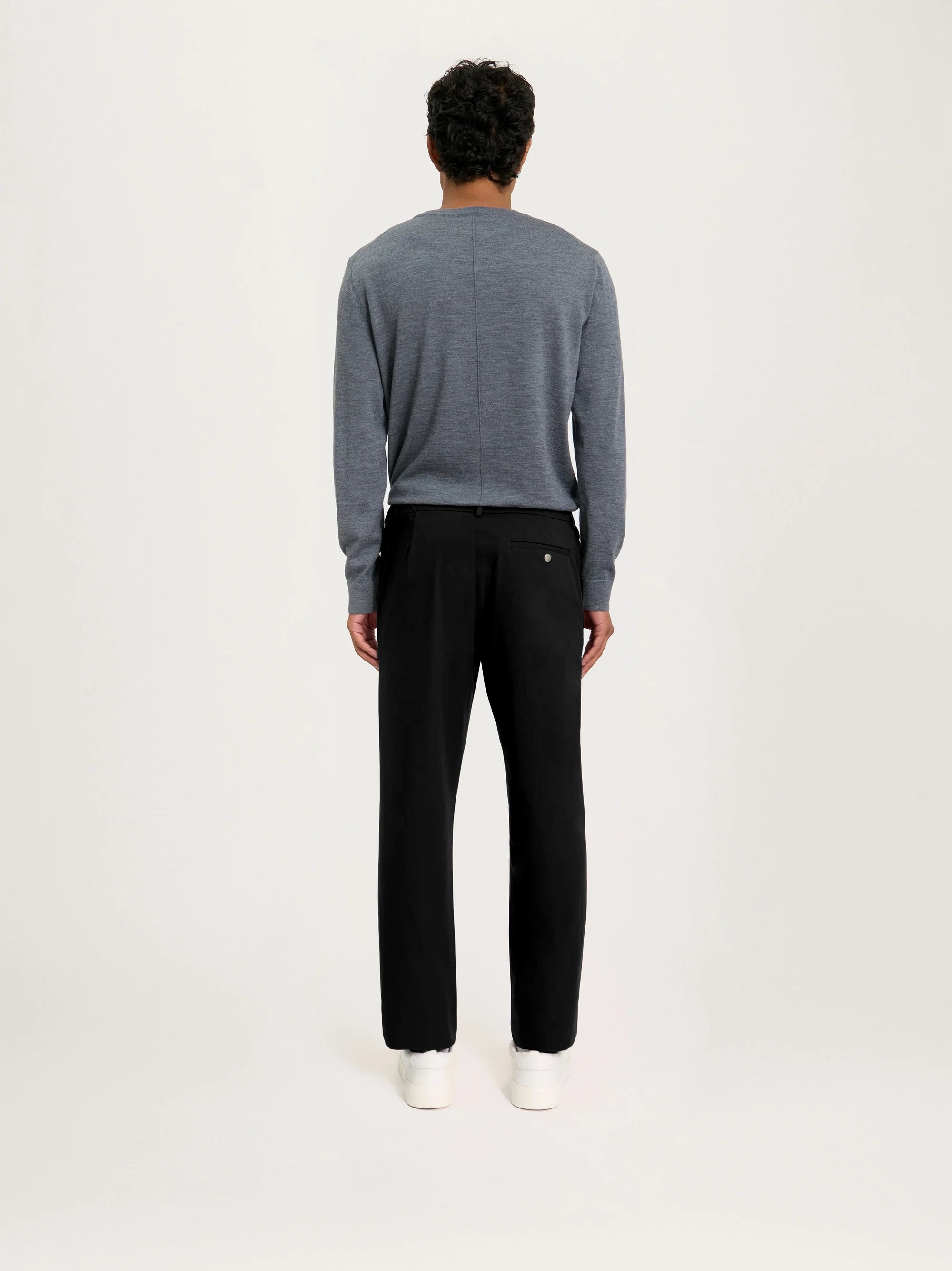 Person wearing a gray sweater and black pants on a white background