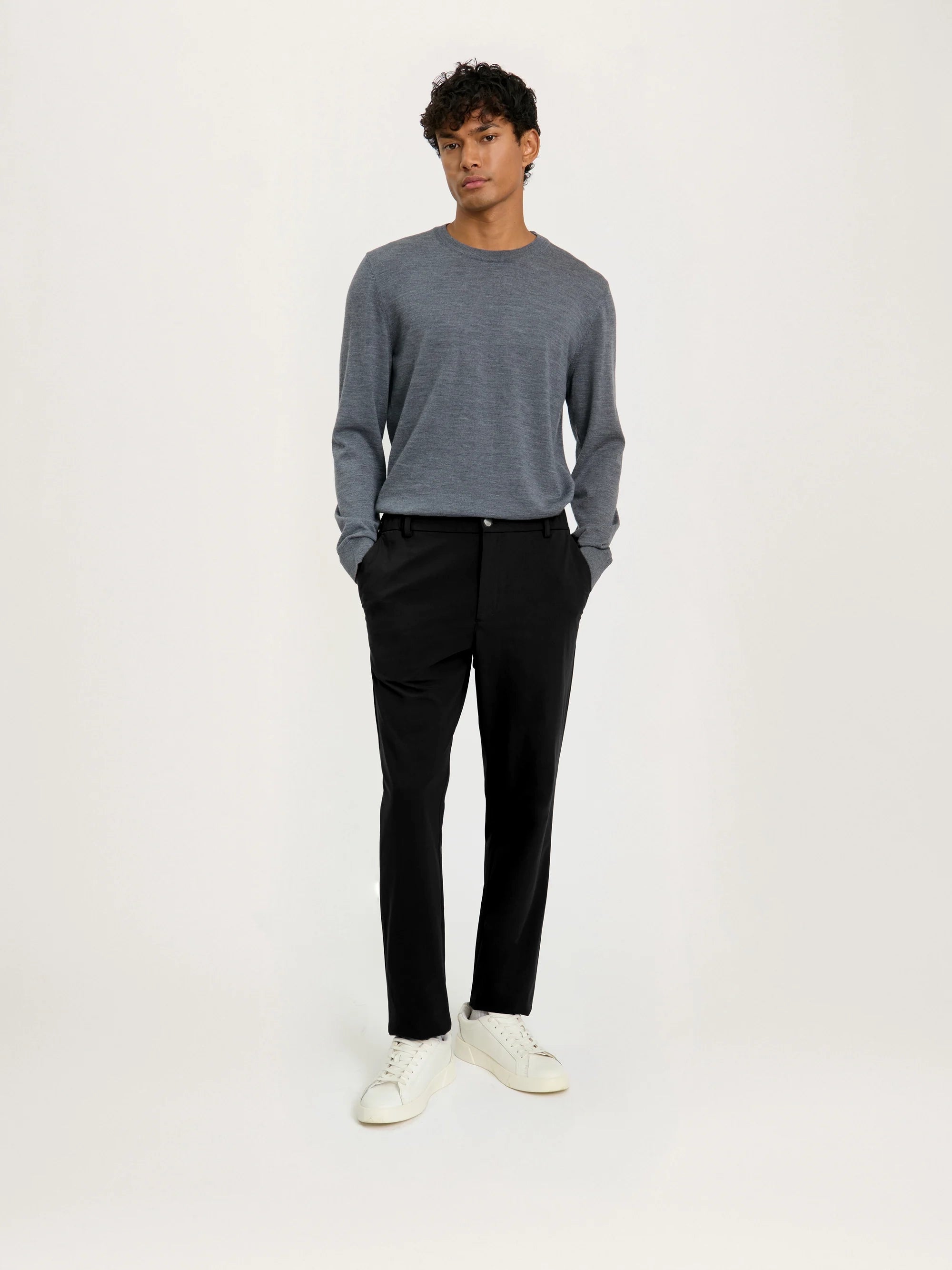 Man wearing a gray sweater and black pants on a white background