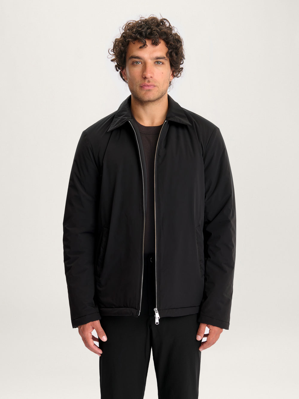 Close-up of model wearing Lestrange 360 Thermal Jacket in black, minimalist insulated outerwear with pointed collar and silver zipper.