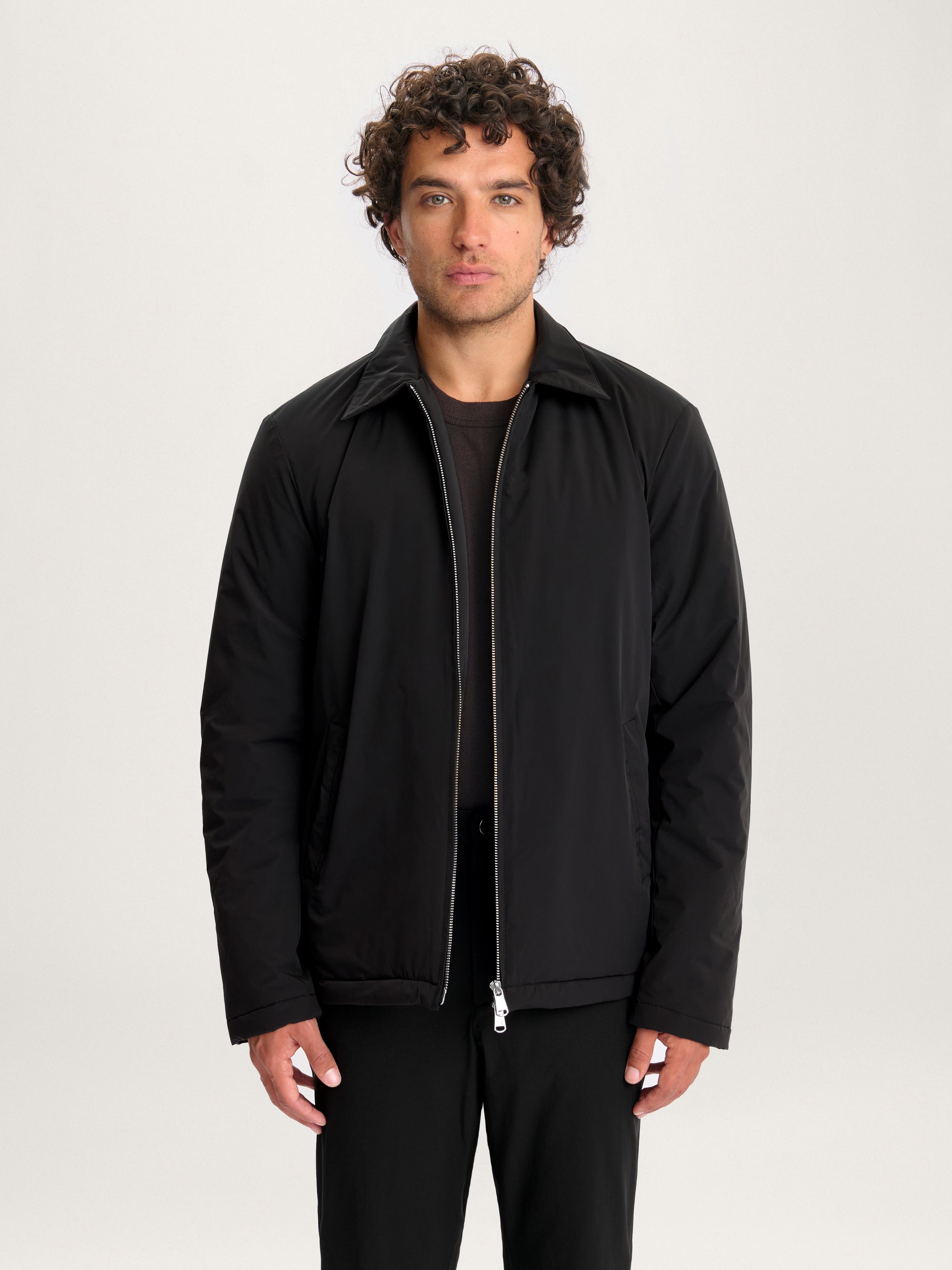 Close-up of model wearing Lestrange 360 Thermal Jacket in black, minimalist insulated outerwear with pointed collar and silver zipper.
