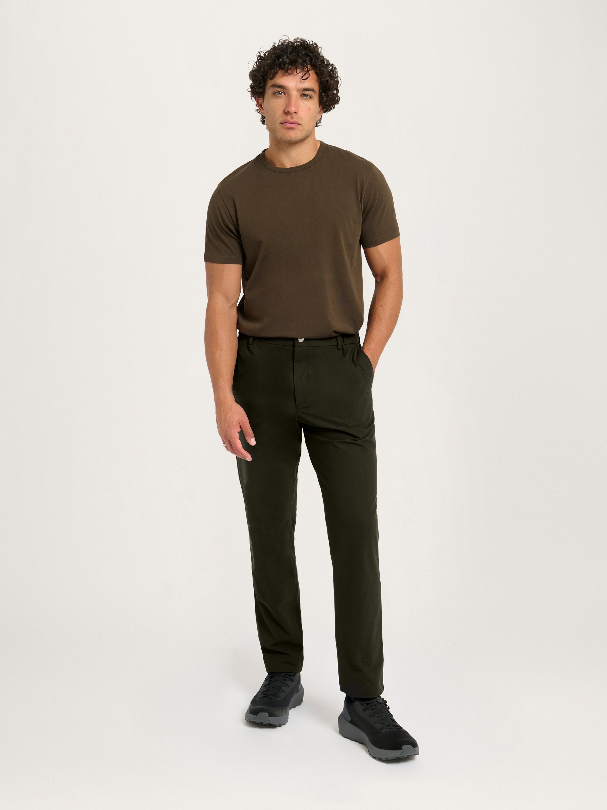 Full-body front view of a model wearing the Lestrange 360 Trouser in Dark Olive paired with a brown T-shirt.