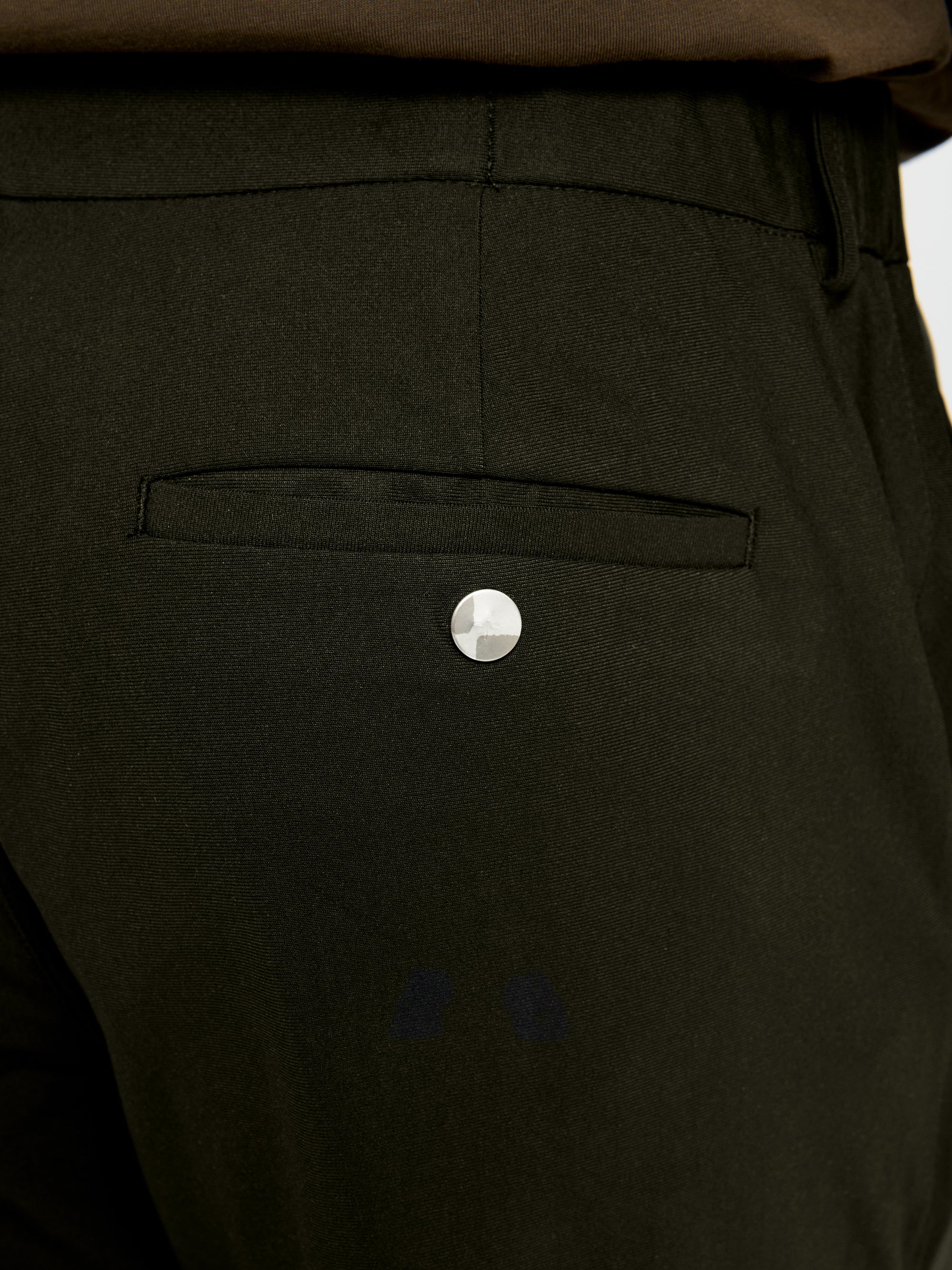 Close-up of the back pocket and silver button detail on the Lestrange 360 Trouser in Dark Olive.