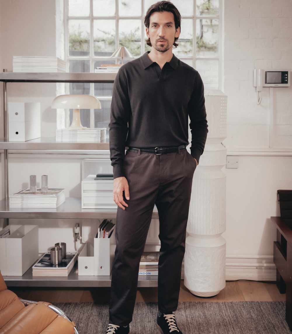 Man wearing Lestrange espresso long sleeve polo shirt and tailored trousers in modern minimalist living room