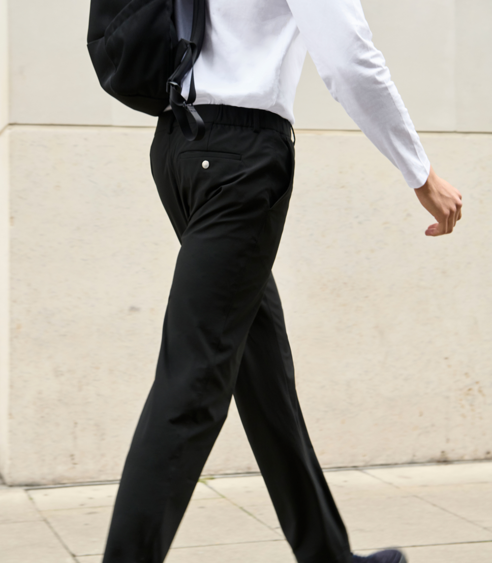Person wearing black pants and a white shirt against a light-colored wall.