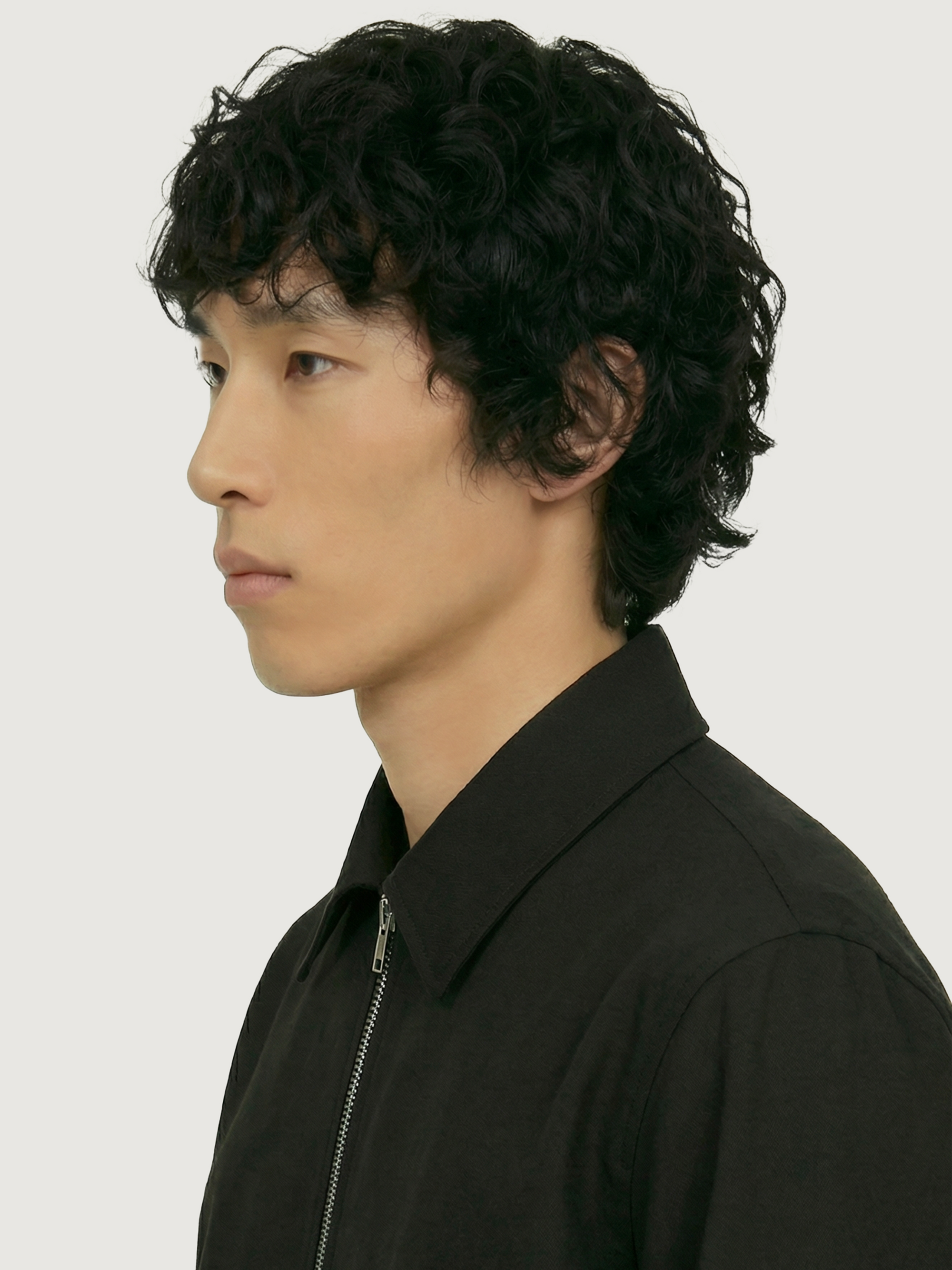 Close-up side profile of The 24 Coach Jacket in black tropical wool, showing the pointed collar, zip front and textured fabric.
