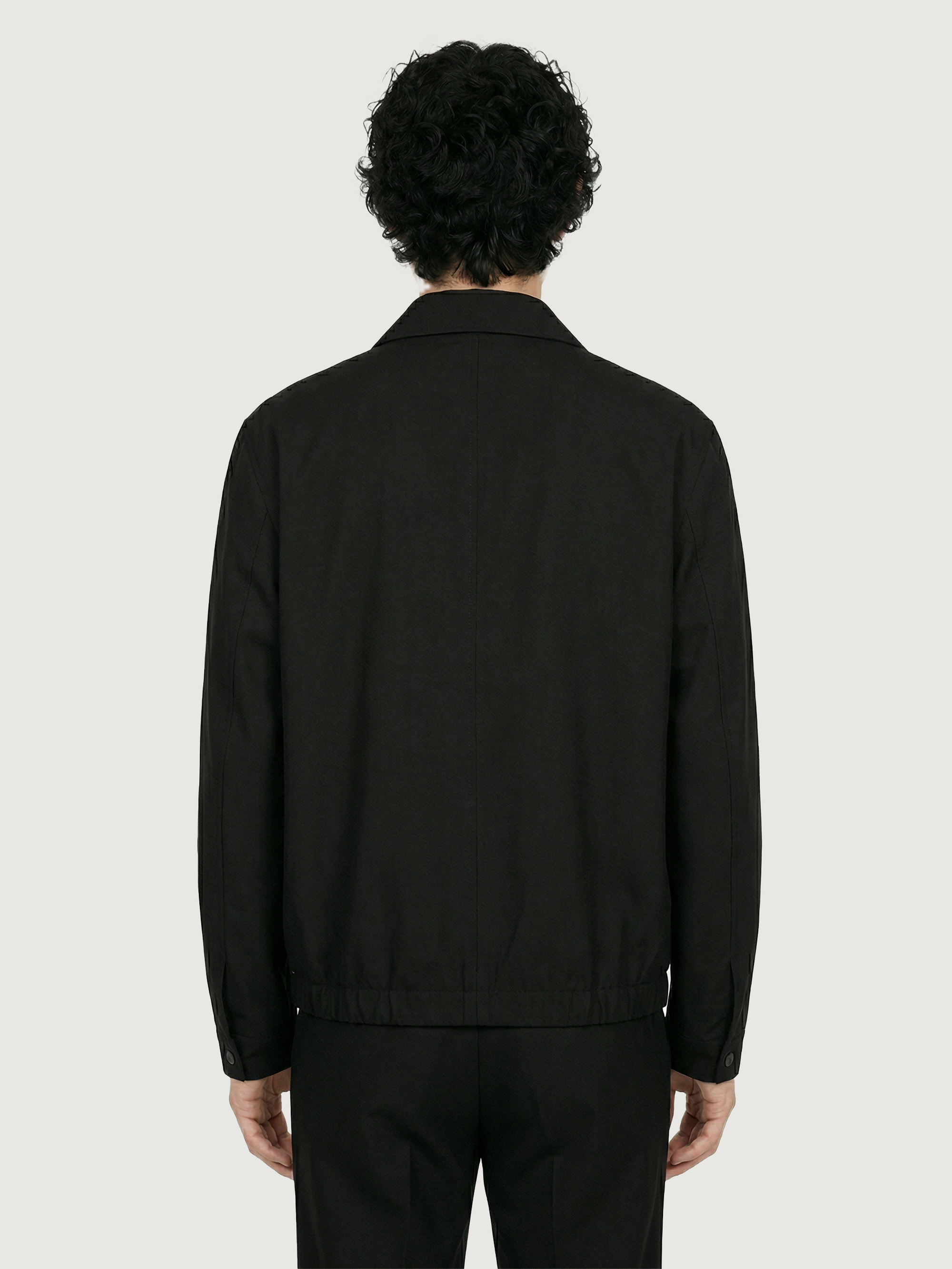 Back view of The 24 Coach Jacket in black tropical wool, showing the relaxed fit, clean back seam and elasticated hem.