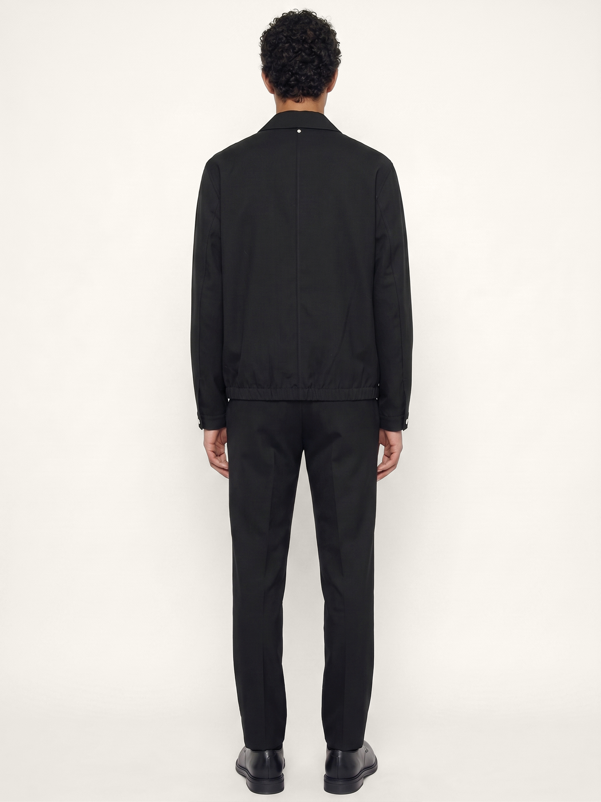 Back view of The 24 Coach Jacket in black tropical wool, showing the clean back seam, elasticated hem and relaxed fit.