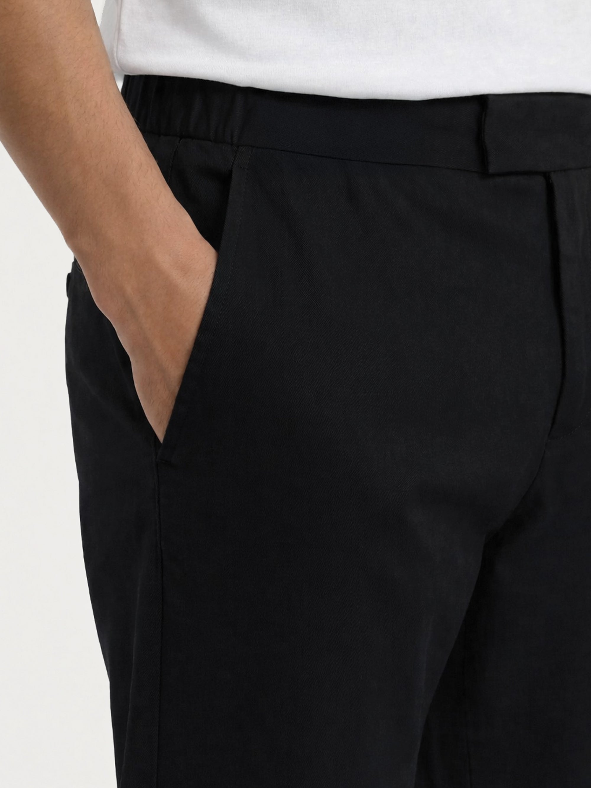 Close-up detail of LESTRANGE black trousers, showing the waistband, side pocket, belt loop, and textured black fabric.