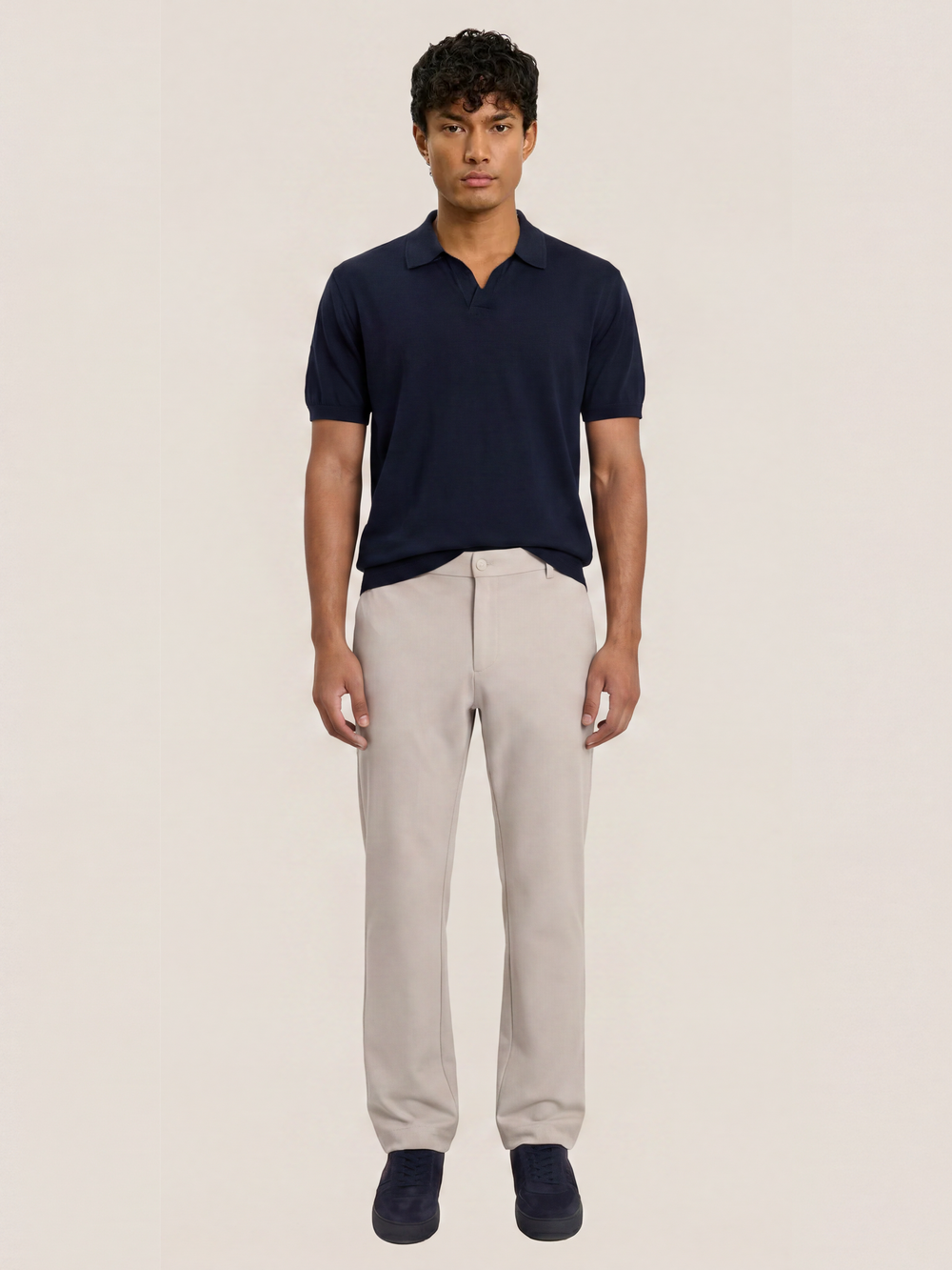Front view of the LESTRANGE 360 Trouser in beige, styled with a navy polo shirt and matching navy trainers.