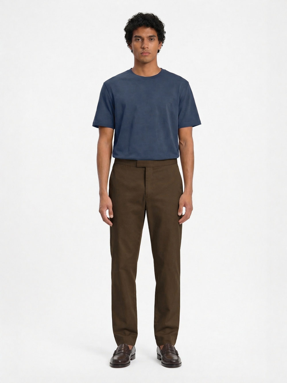 Male model wearing LESTRANGE khaki trousers with a relaxed straight-leg fit, styled with a navy T-shirt and loafers
