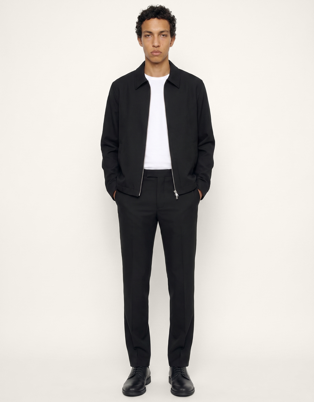 Front view of The 24 Coach Jacket in black tropical wool, styled open over a white T-shirt with matching black trousers.