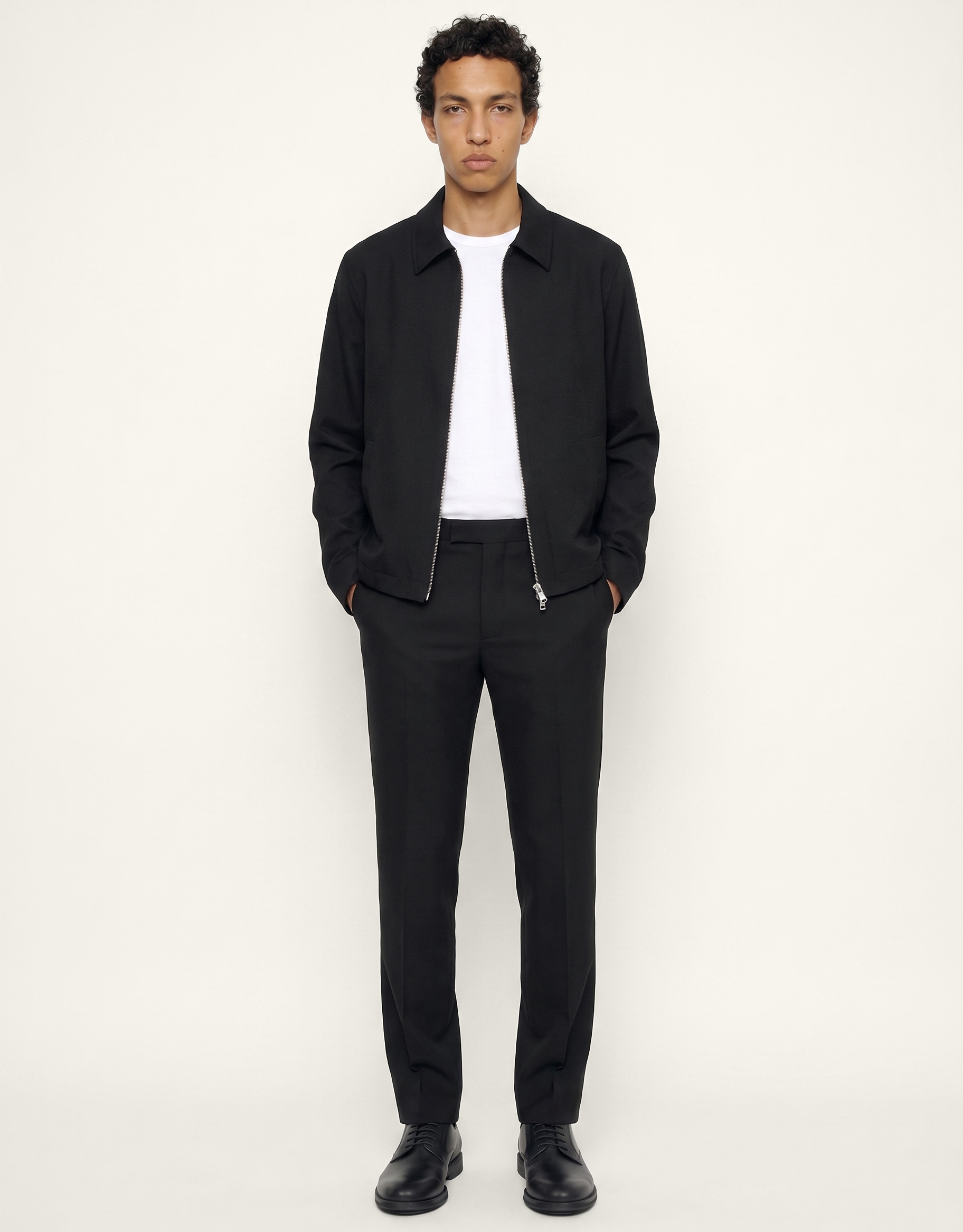 Front view of The 24 Coach Jacket in black tropical wool, styled open over a white T-shirt with matching black trousers.