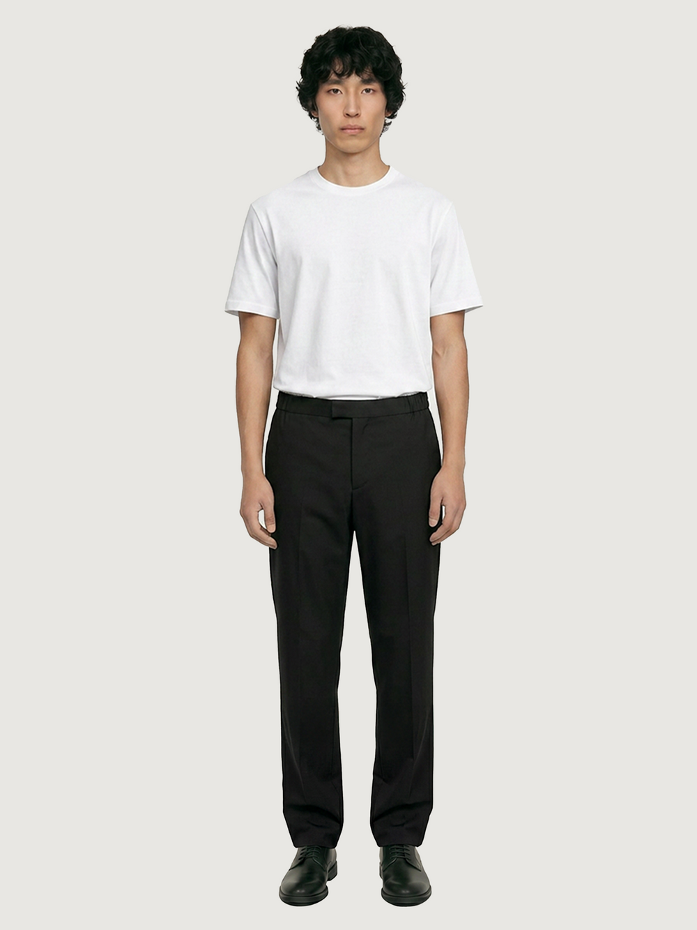 Front view of the LESTRANGE black tropical wool trousers styled with a white T-shirt and black leather shoes.