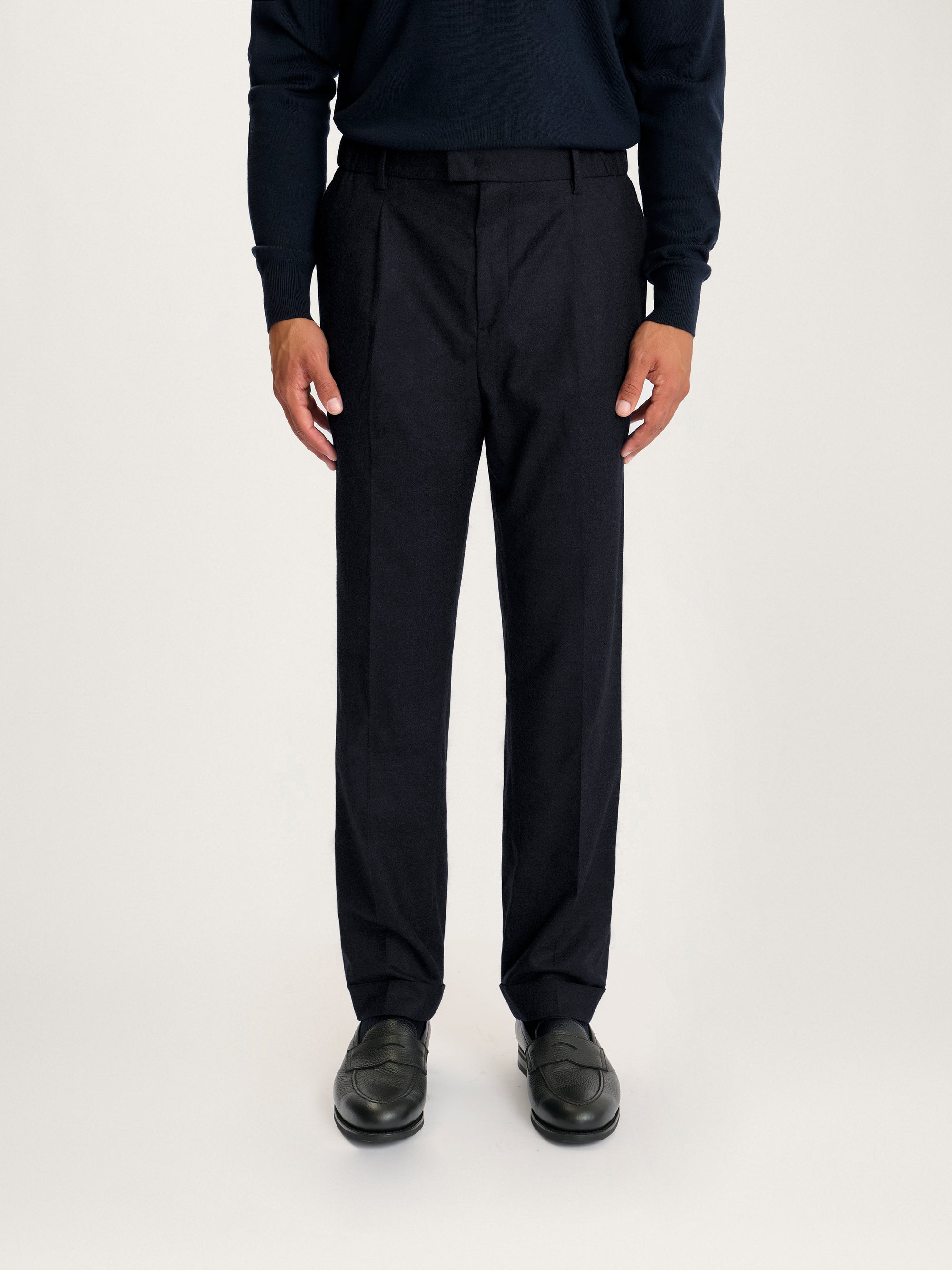 Front view of Lestrange Pleated Wool Trousers in navy, tailored fit with front pleats and a smart pressed crease, styled with black loafers and a navy knit top.