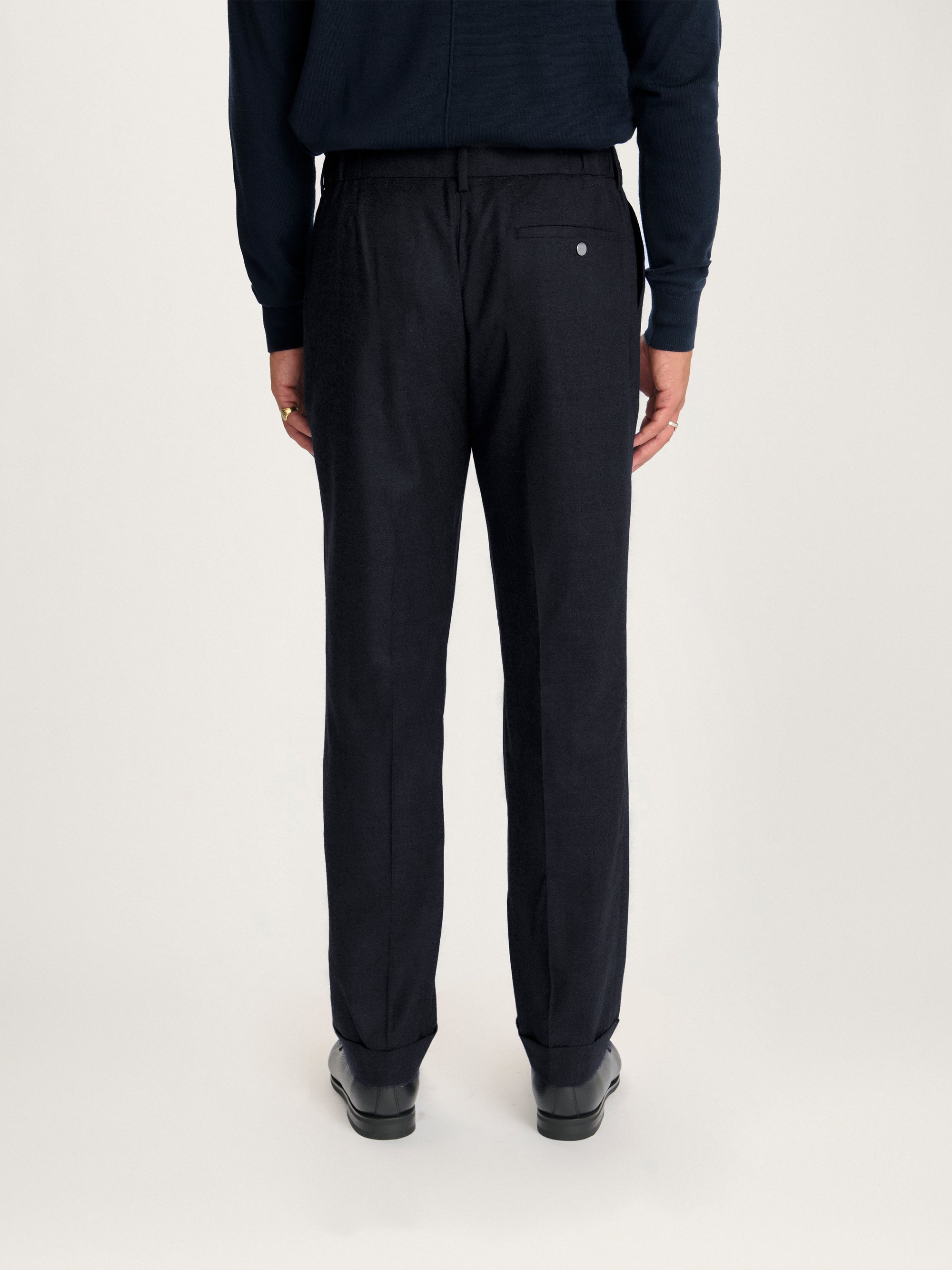 Rear view of Lestrange Pleated Wool Trousers in navy, featuring a single welt pocket with button and tailored cuffed hems.