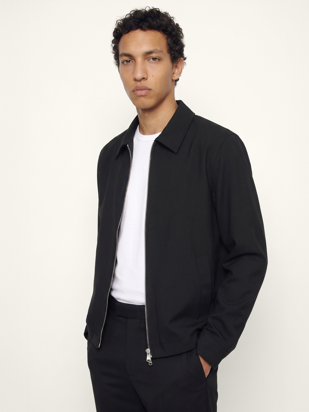 Side view of The 24 Coach Jacket in black tropical wool, showing the zip front, pointed collar and side pocket detail.