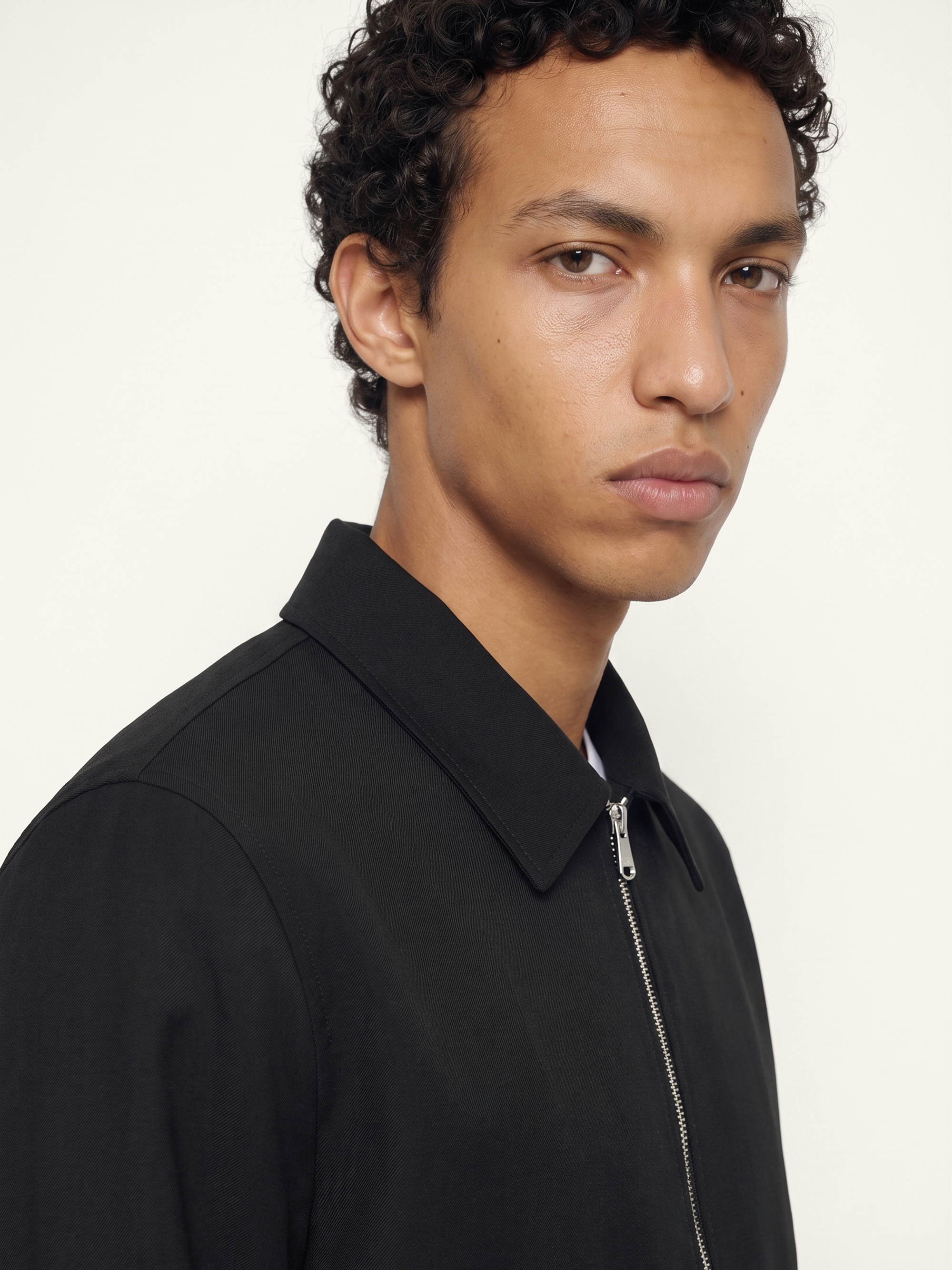 Close-up of The 24 Coach Jacket in black tropical wool, showing the pointed collar, zip fastening and smooth fabric texture.